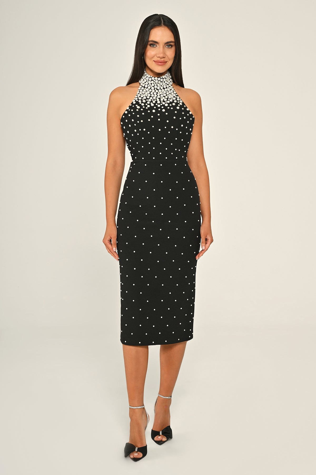 A plus-size model wearing a sleeveless, high-neck, midi dress with pearl embellishments and an open back.