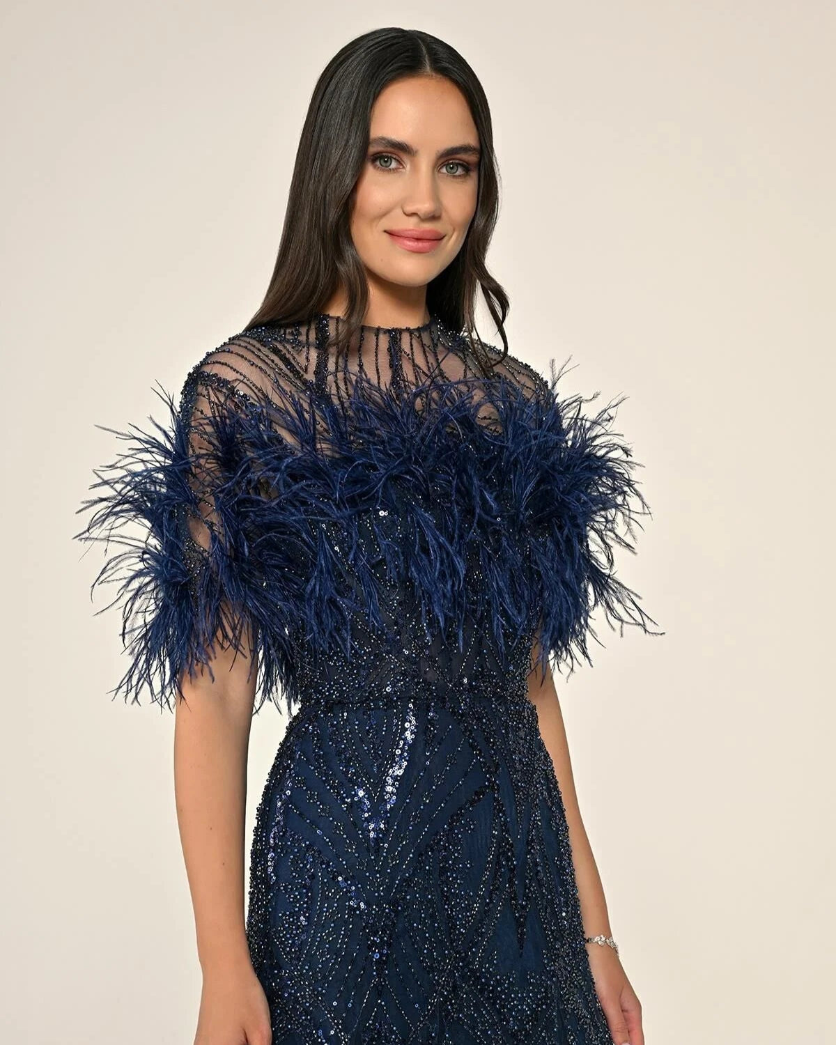 Woman wearing a navy blue dress with feather details on a beige background