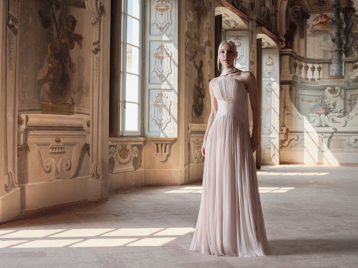 Woman in a elegant dress standing in an ornate room with high ceilings and large windows.