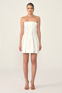Woman wearing a white strapless dress with button details on a plain background
