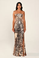 A woman modeling a strapless, floor-length sequined gown in a metallic rose gold tone against a plain light beige studio background.