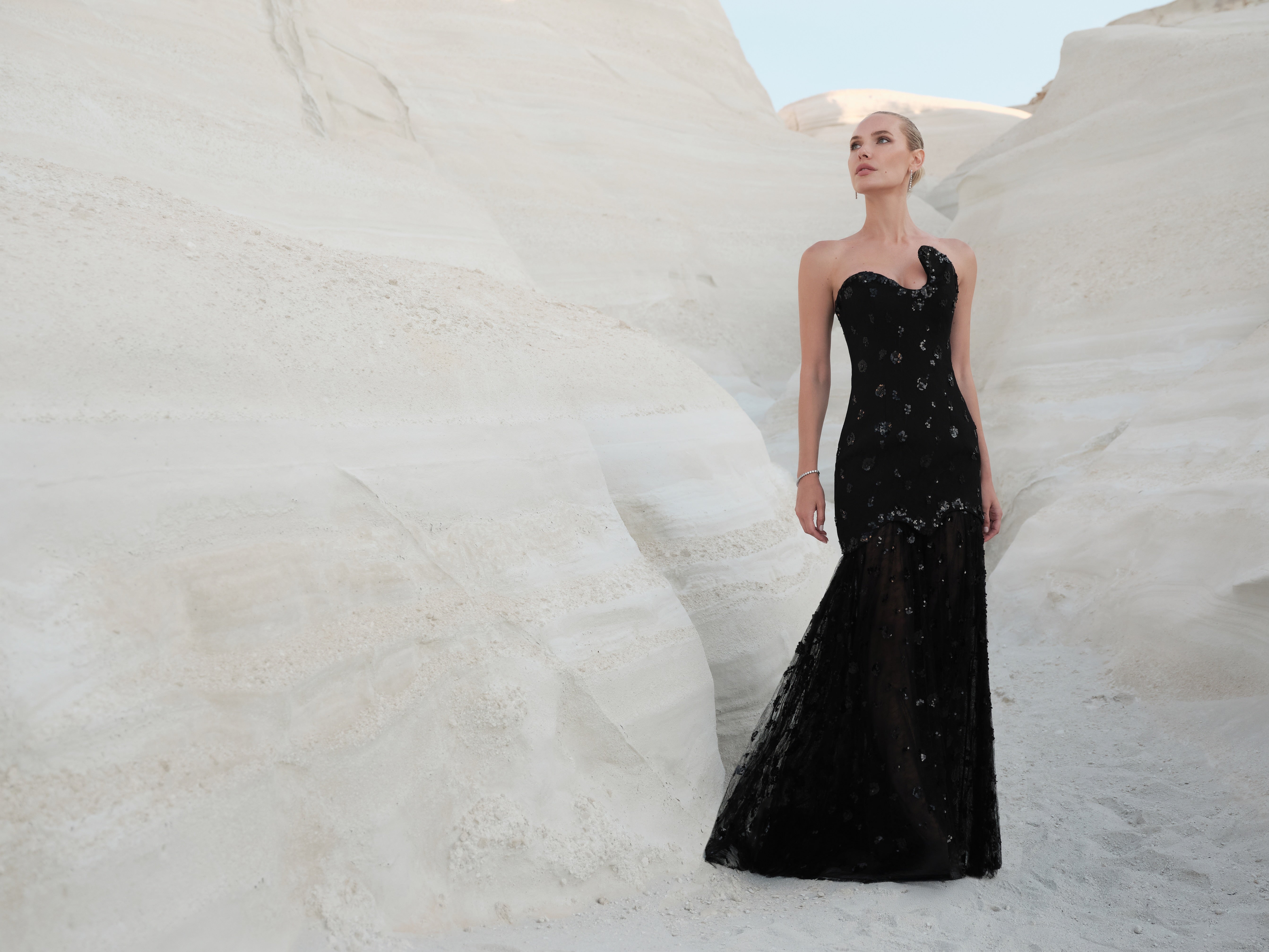 Woman in a black evening gown standing against a white textured wall