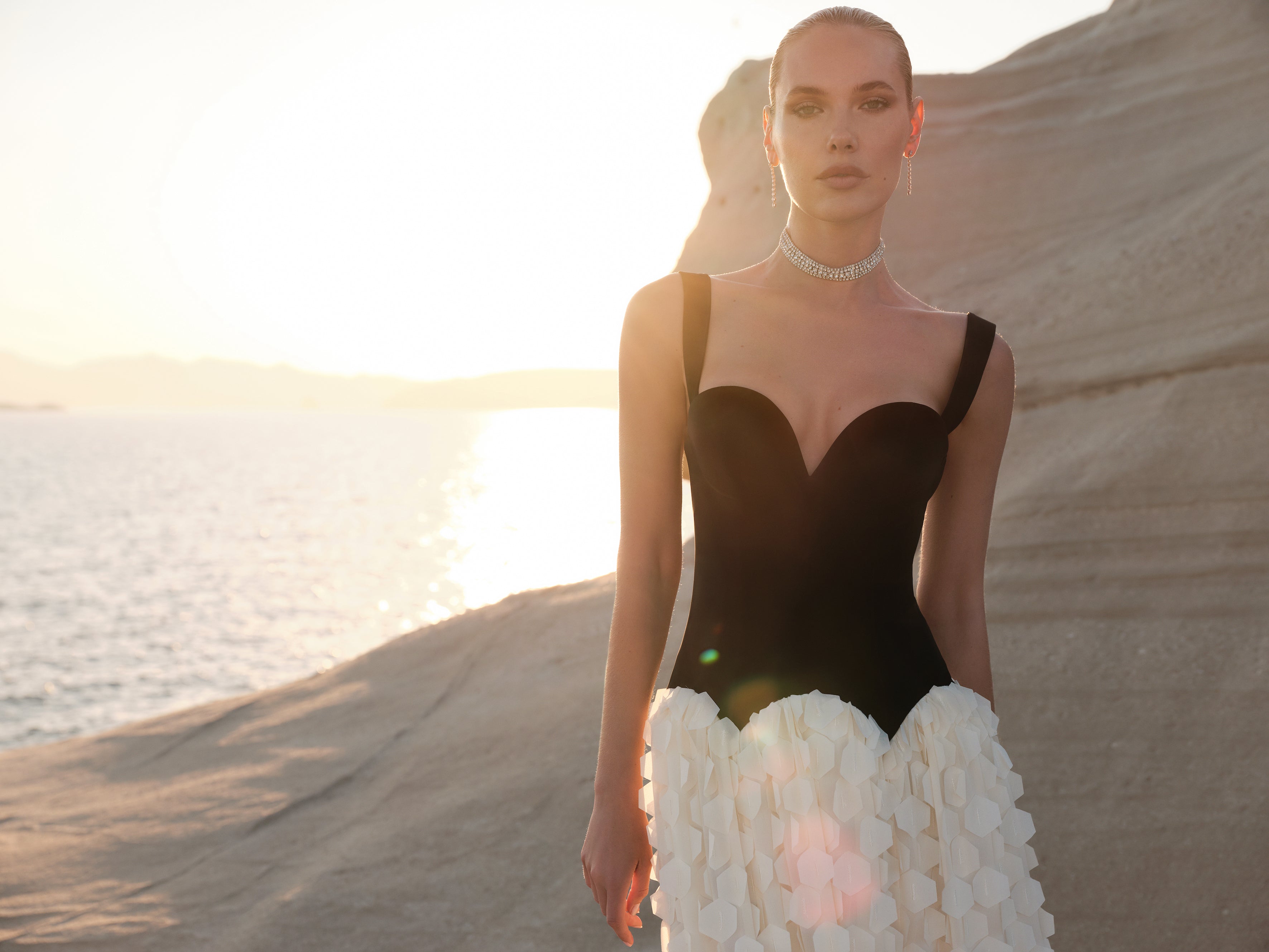 Woman in a black and white dress standing in a desert landscape with sunset.