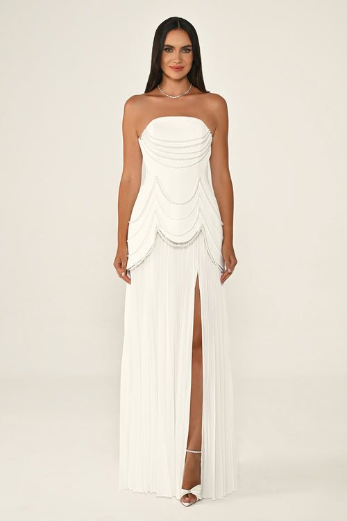 Woman wearing a strapless white gown with a slit on a plain background