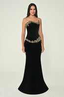 Black strapless evening gown with gold embellishments on a neutral background