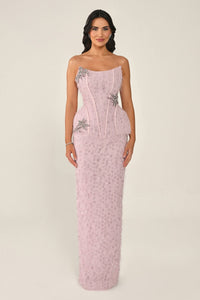 Woman wearing a pink strapless gown with floral embellishments on a beige background