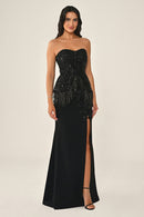 Woman wearing a black strapless gown with fringe details on a beige background