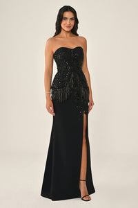 Woman wearing a black strapless gown with fringe details on a beige background