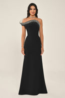 Woman wearing a black evening gown with silver embellishments on a beige background