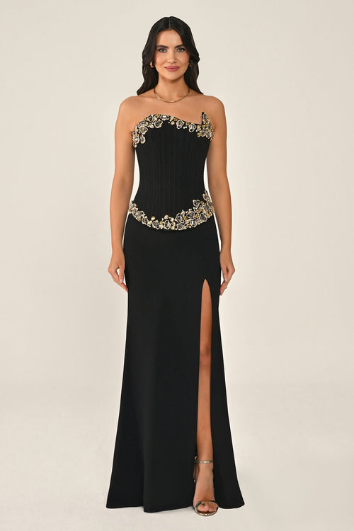 Woman wearing a black evening gown with gold embellishments on a beige background