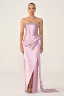 Woman wearing a strapless pink evening gown with a slit on a white background