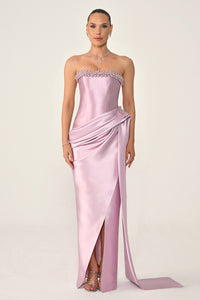Woman wearing a strapless pink evening gown with a slit on a white background