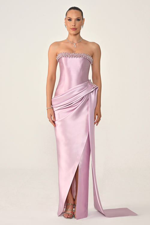 Woman wearing a strapless pink evening gown with a slit on a white background