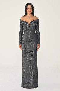 Woman wearing a long, dark gray off-shoulder dress with intricate detailing on a white background