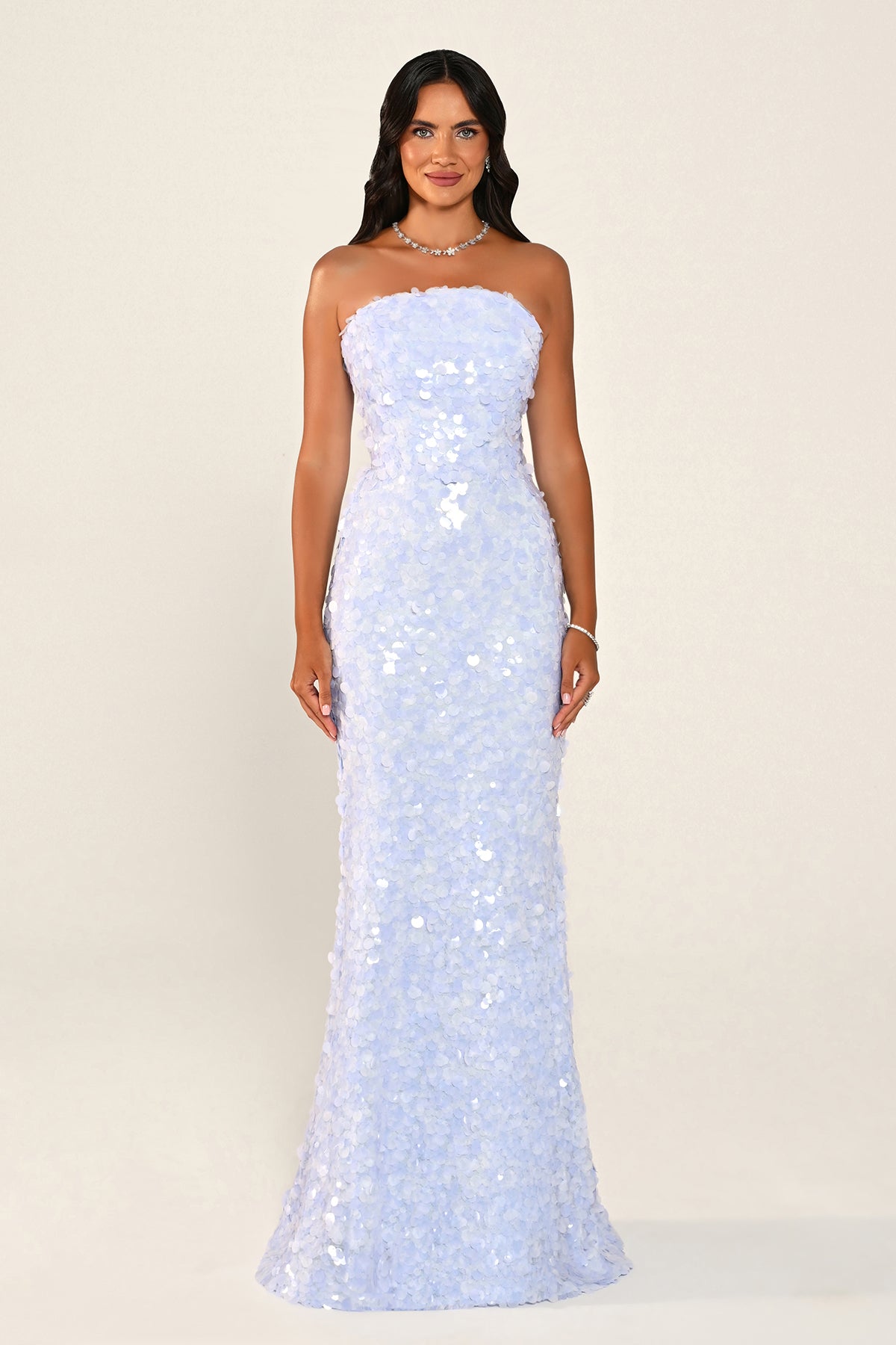 A woman modeling a strapless light blue sequined gown against a plain cream studio background.