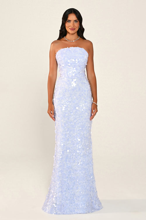 A woman modeling a strapless light blue sequined gown against a plain cream studio background.