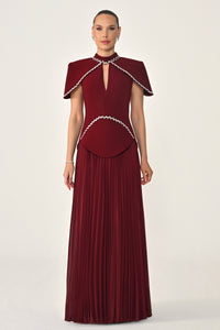 Woman wearing a burgundy evening gown with a white embellished neckline on a white background