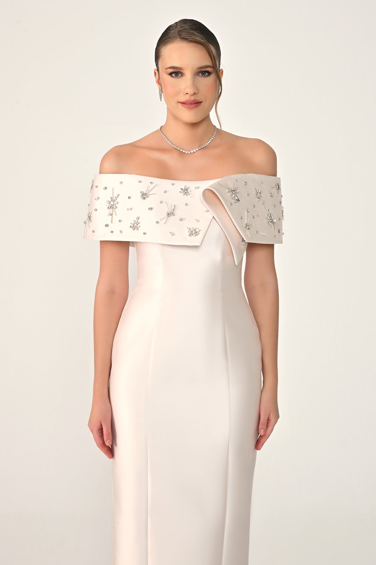 Woman wearing a white off-shoulder dress with intricate detailing on a plain background