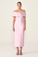 Woman wearing a pink off-shoulder dress with floral embellishments on a white background