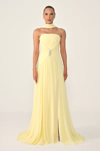 Woman wearing a light yellow strapless gown on a plain background