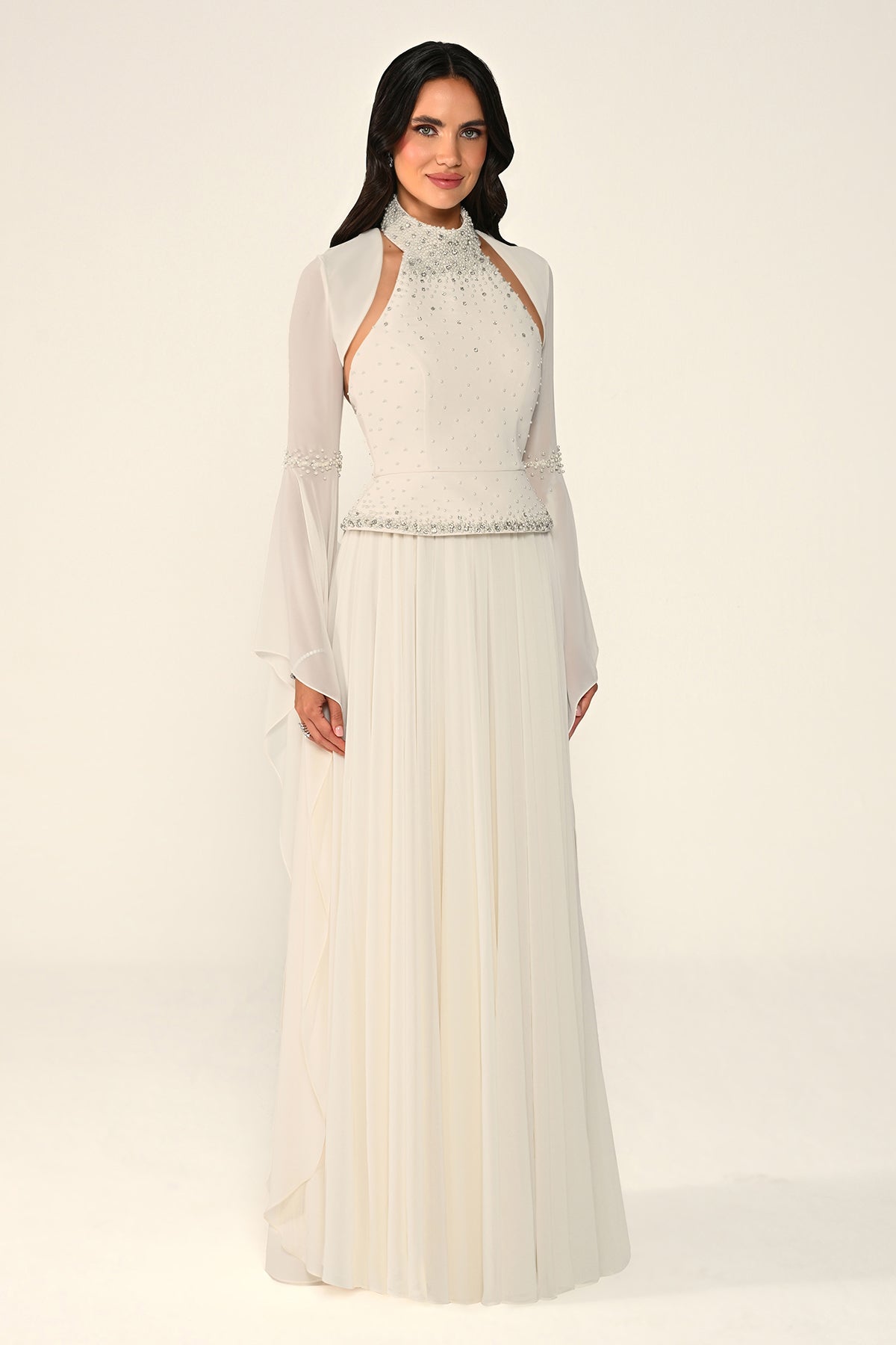 Woman wearing a long, light-colored dress with sheer sleeves against a white background