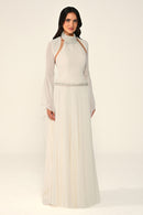 Woman wearing a long, light-colored dress with sheer sleeves against a white background