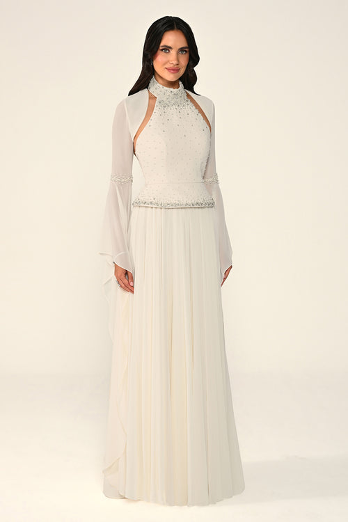 Woman wearing a long, light-colored dress with sheer sleeves against a white background