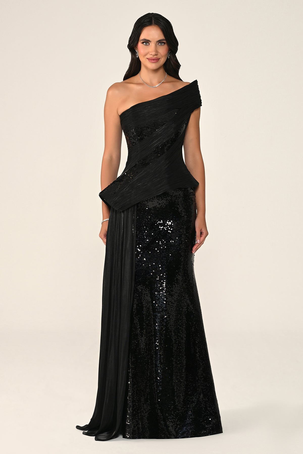 Woman wearing a black one-shoulder evening gown with sequin details on a beige background