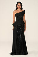 Woman wearing a black one-shoulder evening gown with sequin details on a beige background