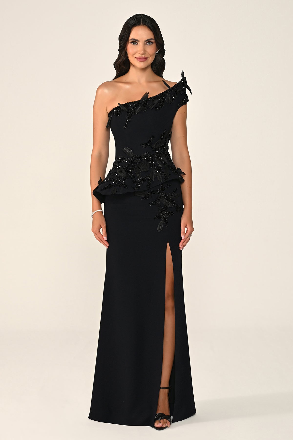 Woman wearing a black one-shoulder evening gown with beading on a beige background