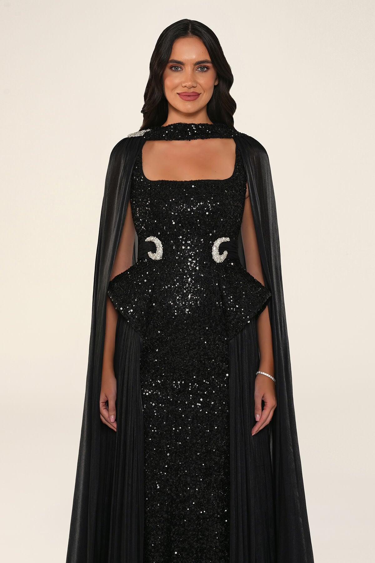 Celestara Dress in Black: sequin column gown with a square neckline, peplum hip detail, stone-embellished waist and a flowing organza cape