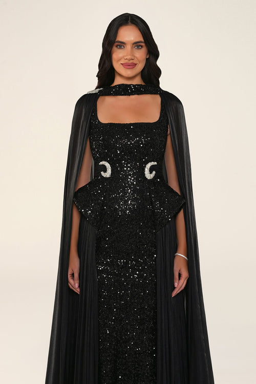 Celestara Dress in Black: sequin column gown with a square neckline, peplum hip detail, stone-embellished waist and a flowing organza cape