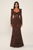 A woman modeling a floor-length brown lace gown with long puff sleeves, a sweetheart neckline, a lace-up corset-style bodice, and a peplum waist, photographed against a plain light beige studio background.