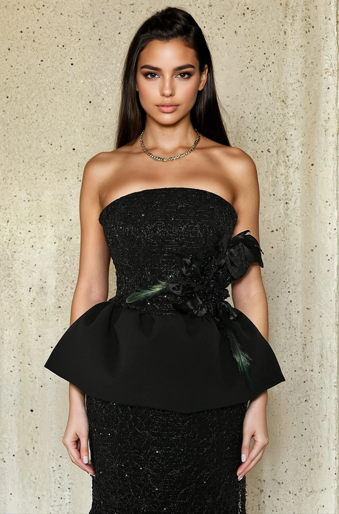 Woman wearing a black strapless dress with floral details against a textured wall.