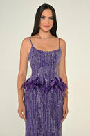 Woman wearing a purple sequin dress with feather details on a beige background