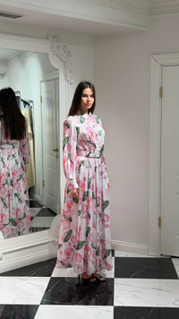 Woman in a floral dress standing in a room with a mirror reflecting her image.