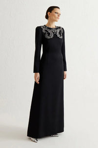 Woman wearing a black evening gown with intricate detailing on a white background