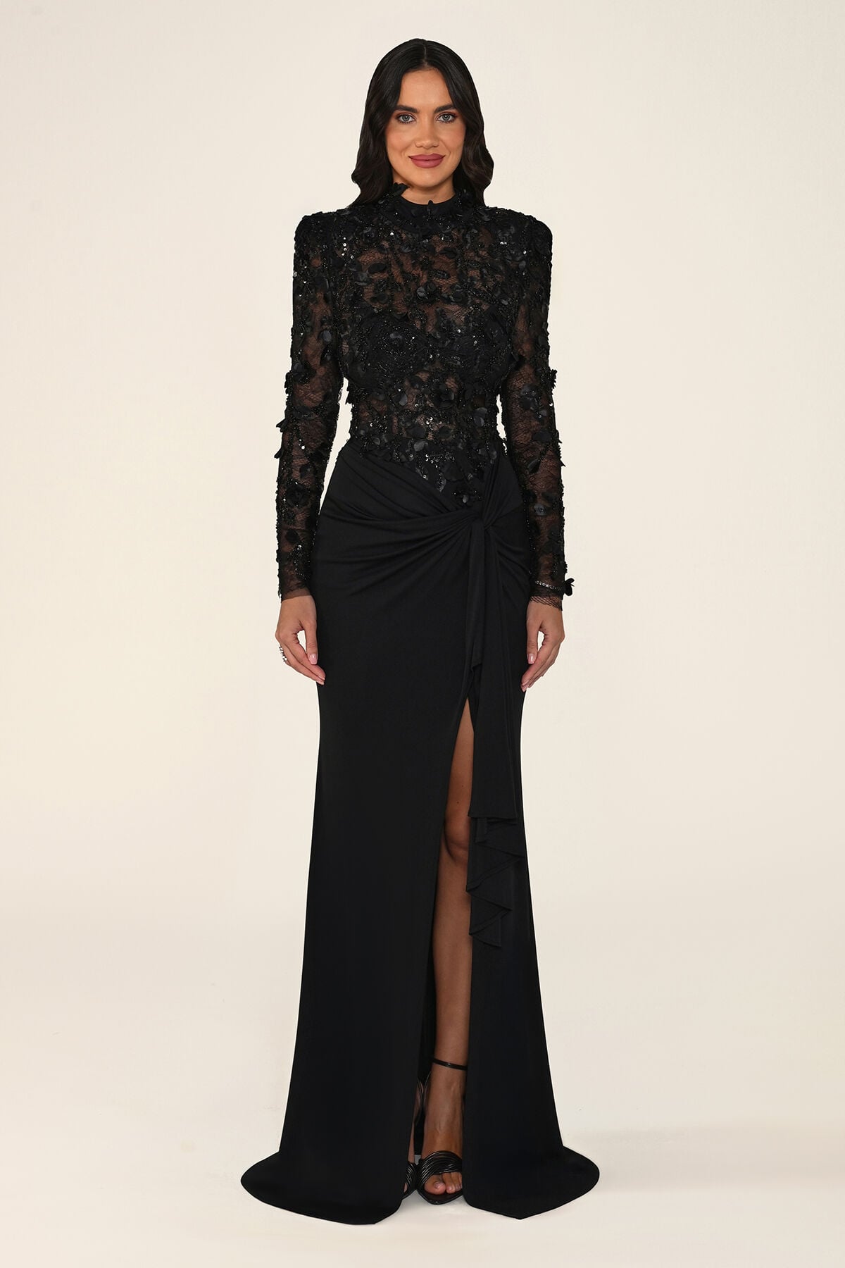 Vespera black maxi evening dress with long sleeves, high neck, sequinned floral lace bodice and tie-waist skirt with leg slit